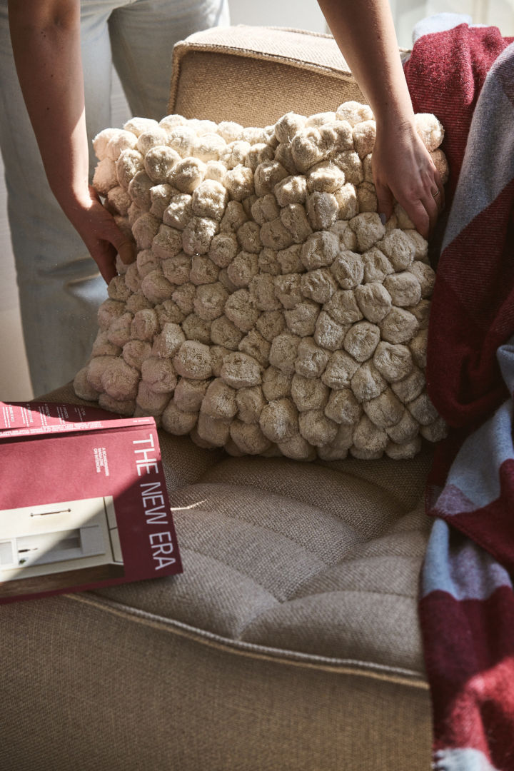 The Pom Pom pillow from Byon seen here being placed on a sofa with a burgundy and blue throw. Textured and structured materials are one of the trends from autumn 2024. 