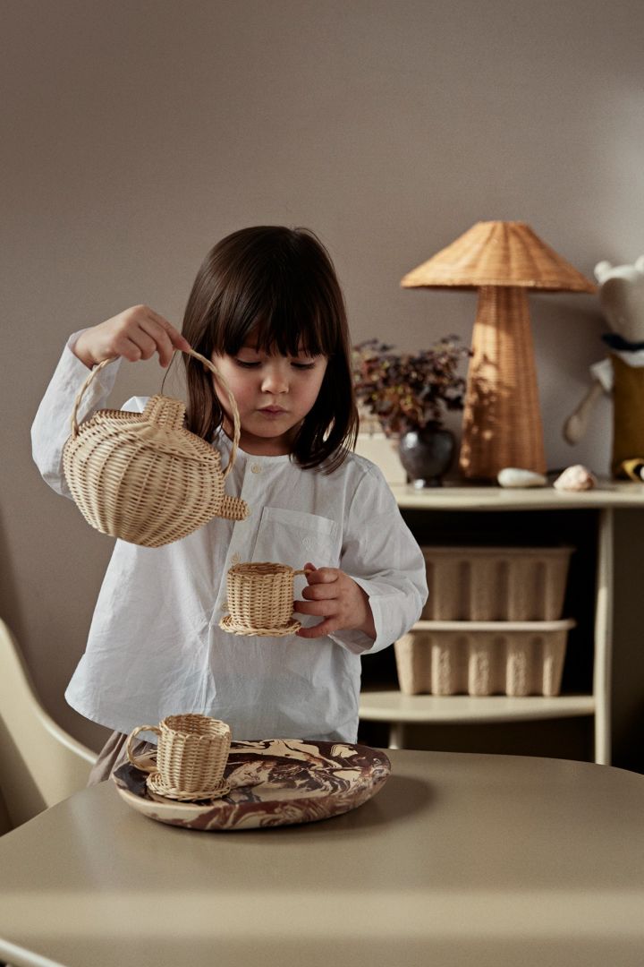 A child pretends to pour tea from a wicker teapot, playful stylish toys are perfect ideas to display in a children's room. 