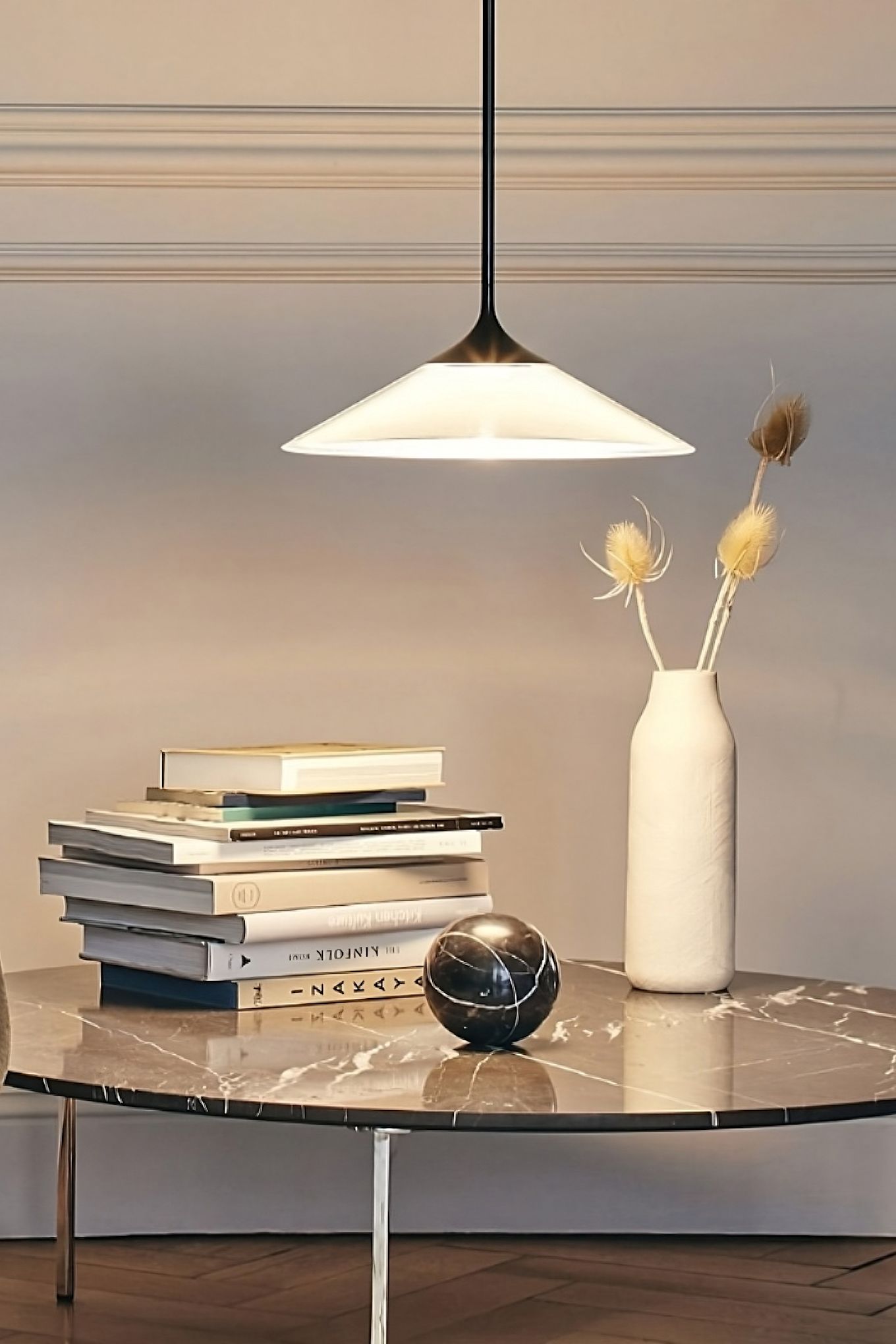 The Orsa ceiling lamp from Artemide hangs over a table with a stack of books and a vase. 