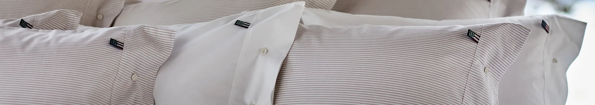 Close-up of neatly stacked pillows with white and striped beige bedding, showing 'Lexington' labels and buttons.