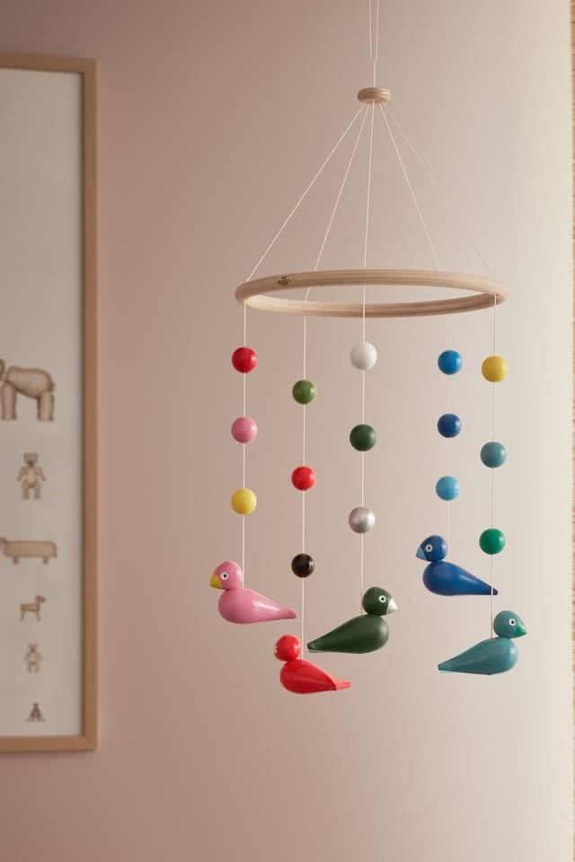 A colourful mobile with birds hangs in a neutral coloured room, mobiles are a great baby shower gift ideas. 