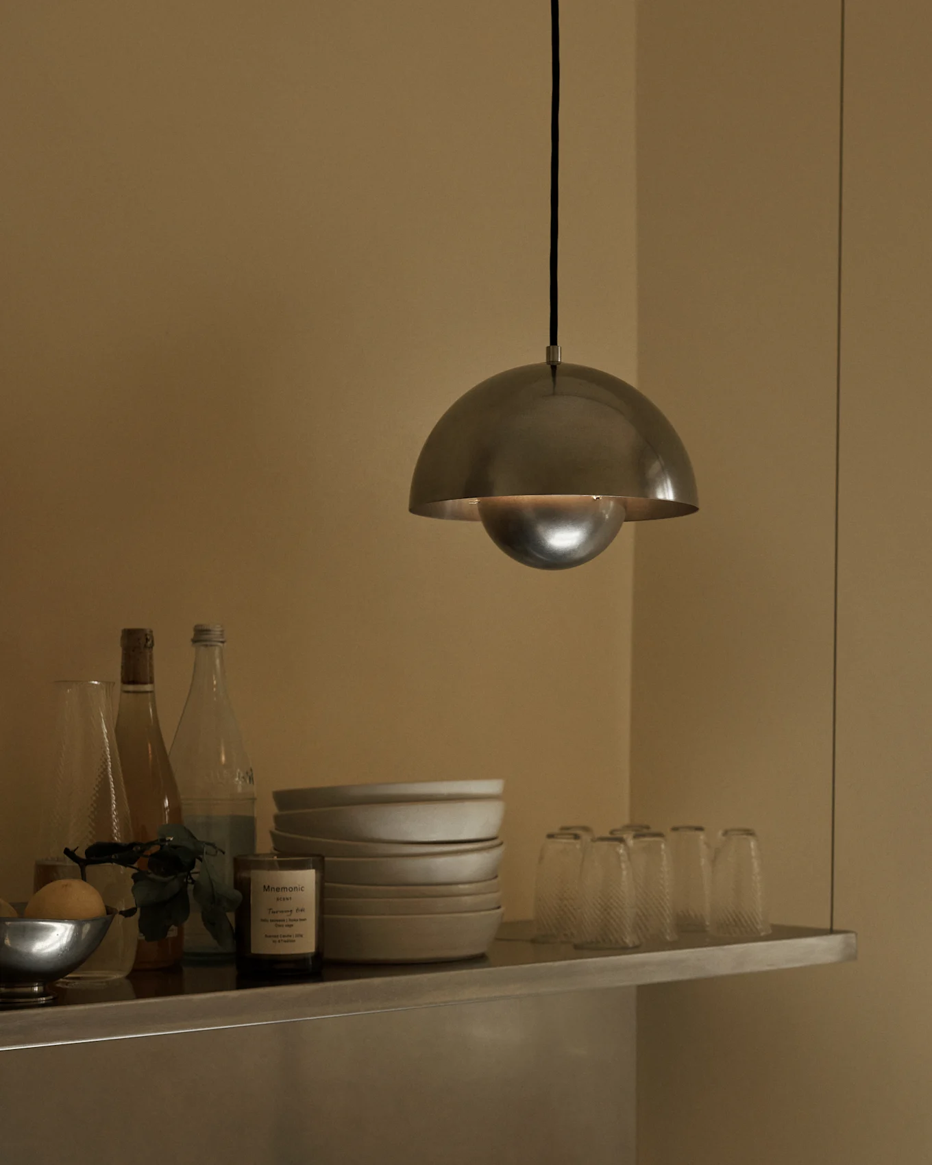 A brushed metal dome pendant light hangs over a shelf with bowls, bottles, and glasses.