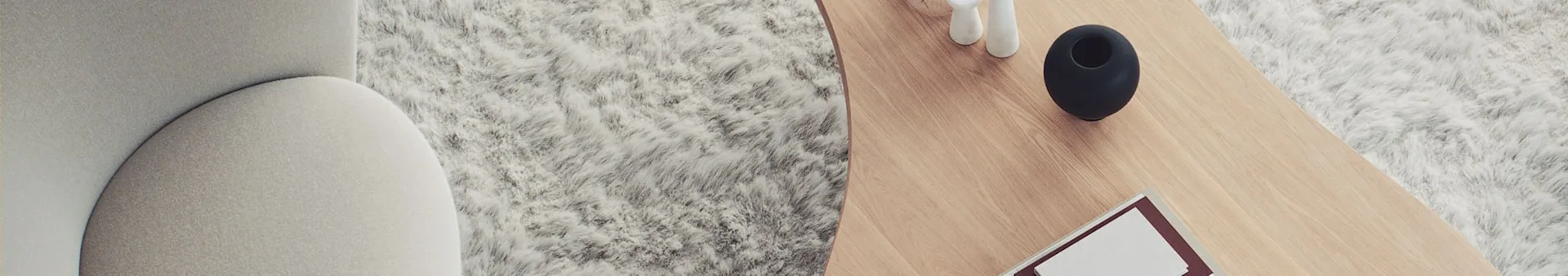 Overhead view of a light couch and fluffy white rug beside a wooden coffee table with a black vase, white decor, and a book.