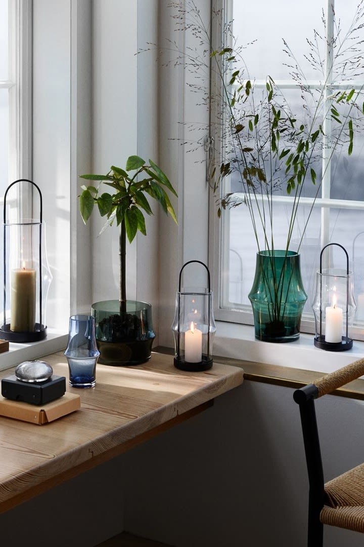 Here you can see a corner window with a small table in front of it, the windowsill is decorated with several Arc lanterns in different sizes with candles, in between are several Arc vases with flowers.