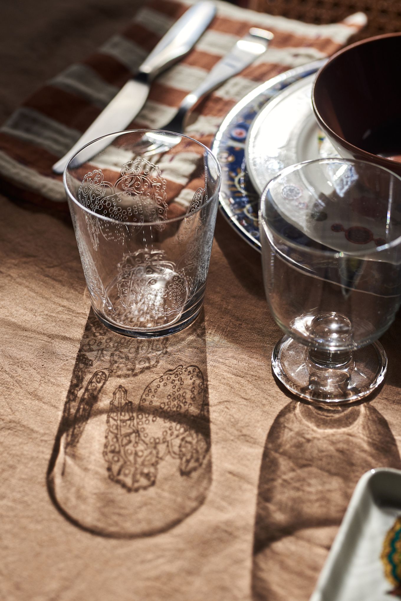 The sun shines through the Taika drinking glass casting a shadow on the table in a bohemian table setting idea. 