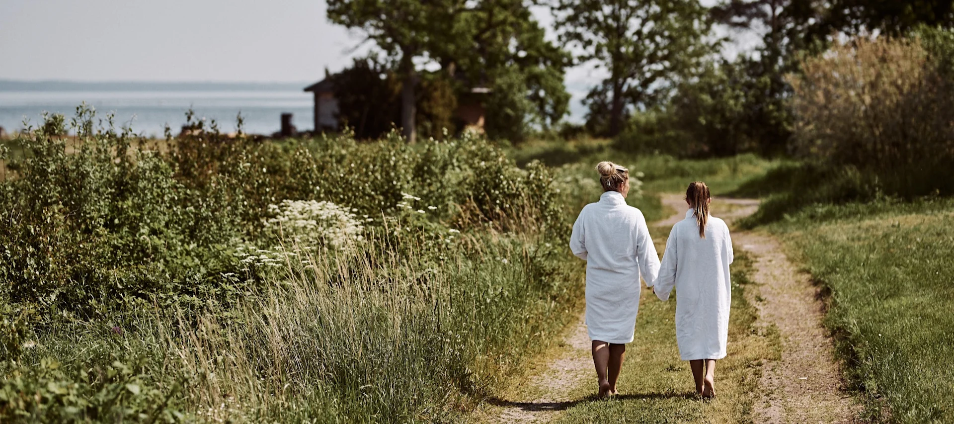A woman and a girl walk to the beach wearing white bathrobes. A dip in the sea is a must do on any Swedish summer bucket list.