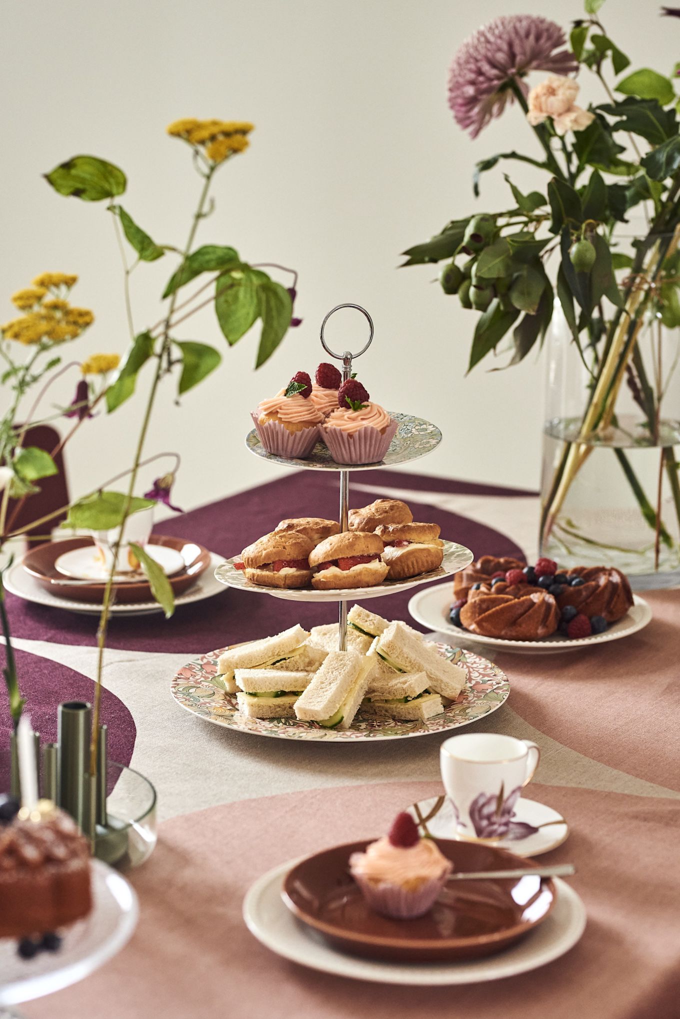 A hand holds a teapot over a table laid out ready for a tea party. 