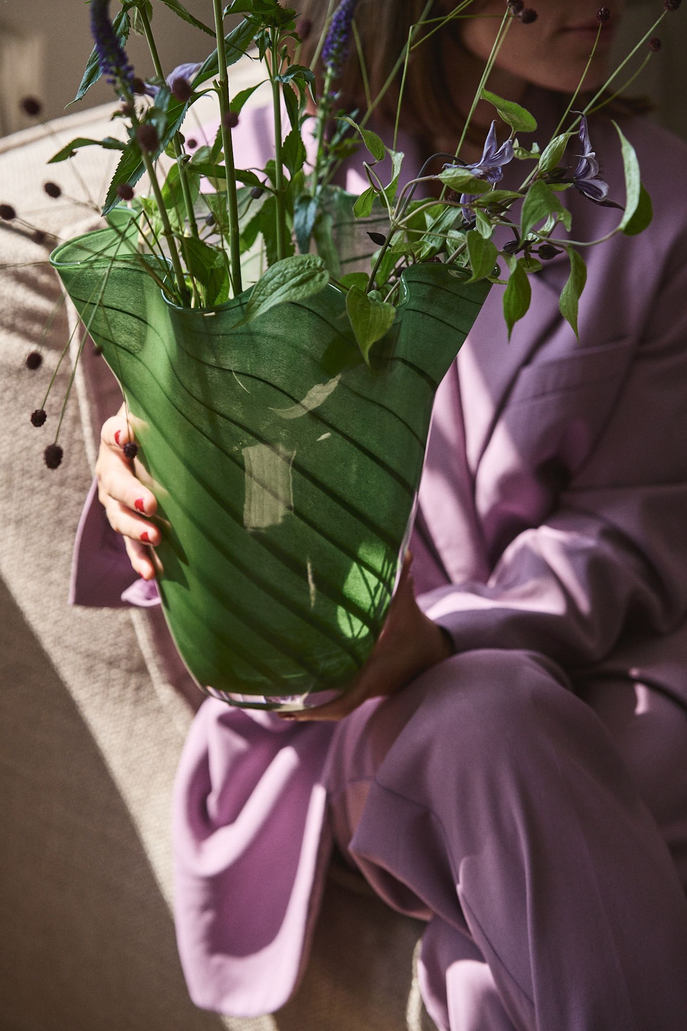 Person wearing purple clothes holding the green glass vase Tiggy from Byon, a vase with a pleated, bell-shaped form in pea green with stripes.