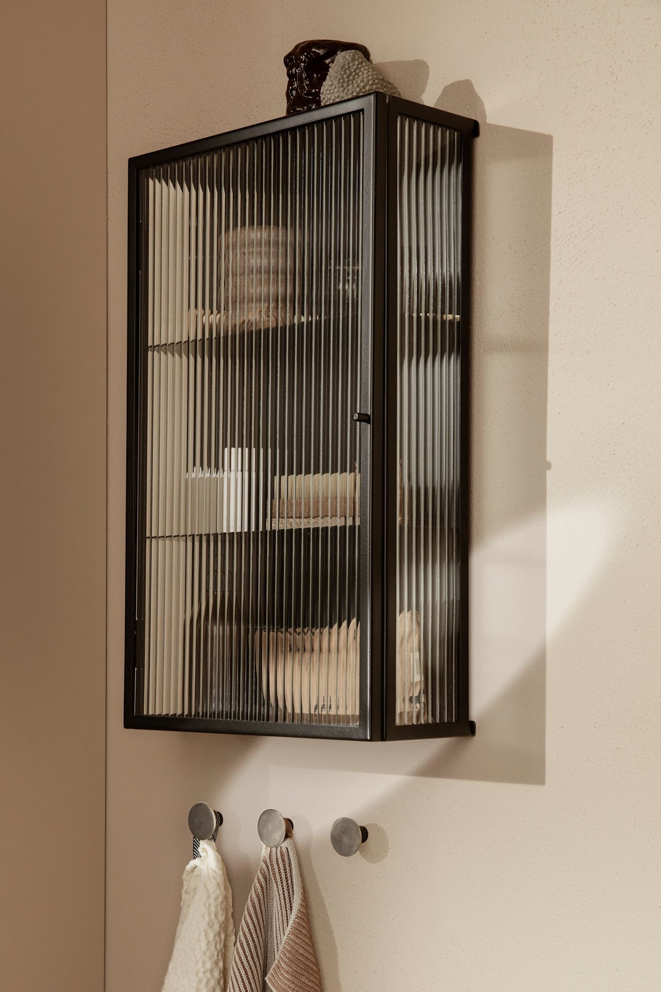 Fluted glass is one of this year's trends. The the Haze wall cabinet from ferm LIVING hangs on the wall in a neutral coloured bathroom. 