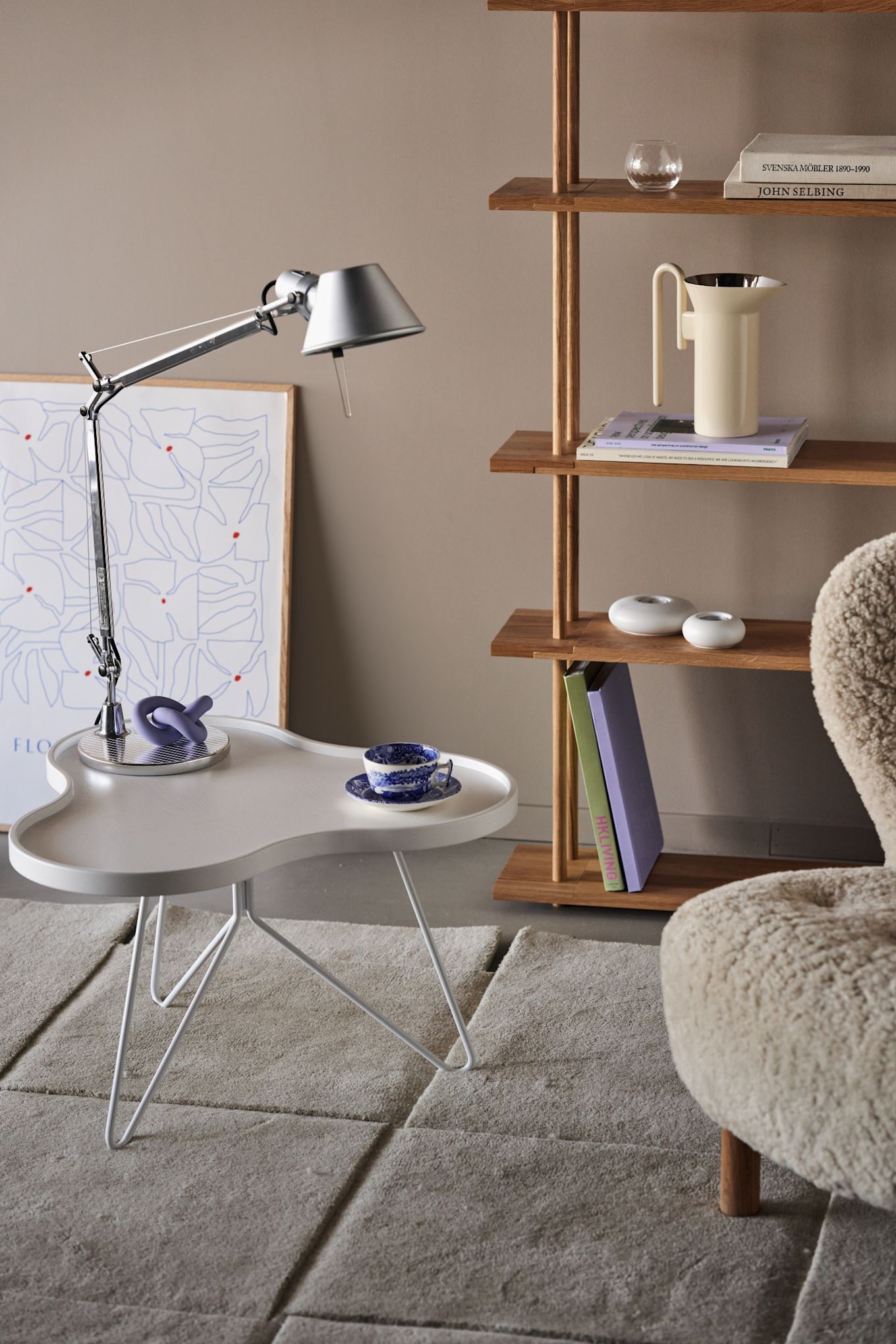 The stainless steel Tolomeo lamp with an adjustable arm stands on a white table with purple accents. 