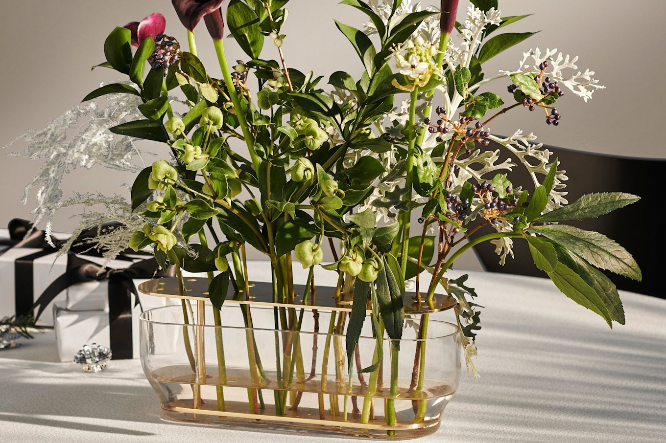 A close up of the long Ikebana vase from Fritz Hansen, with a bunch of green and dark purple flowers.