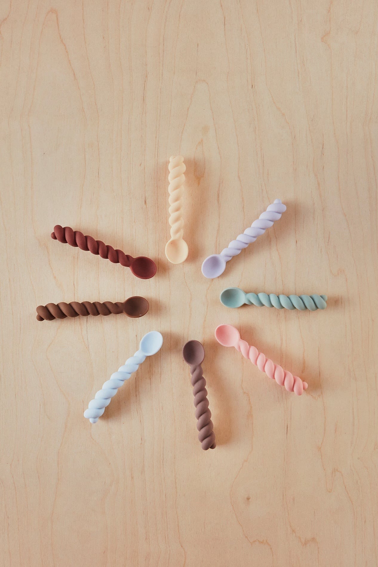 Baby spoons from OYOY with twisted handles are arranged in a circle. Cutlery makes an idea baby shower gift idea. 