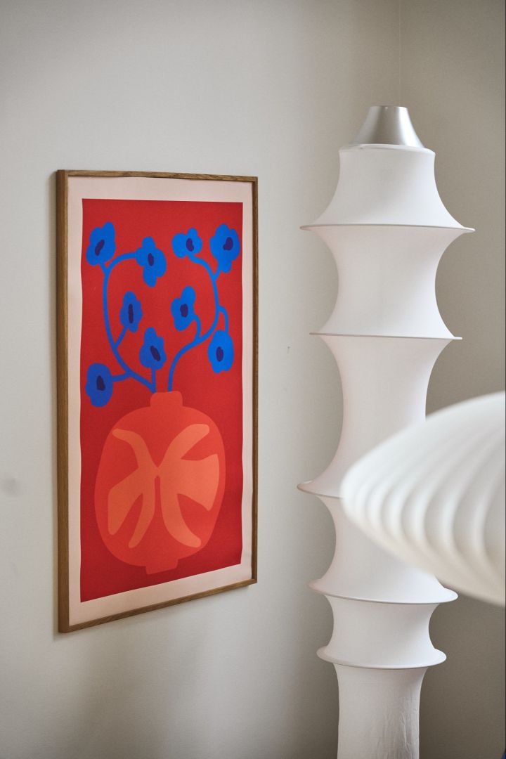 The Falkland floor lamp in white stands next to a red and blue printed poster. 