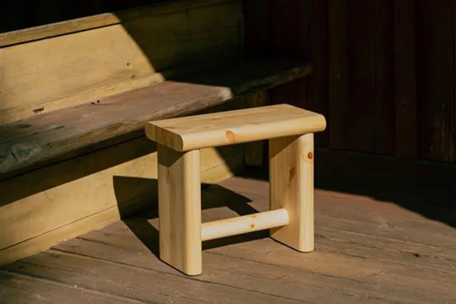 A light wooden stool with rounded edges on a wooden deck, partially lit by sunlight.