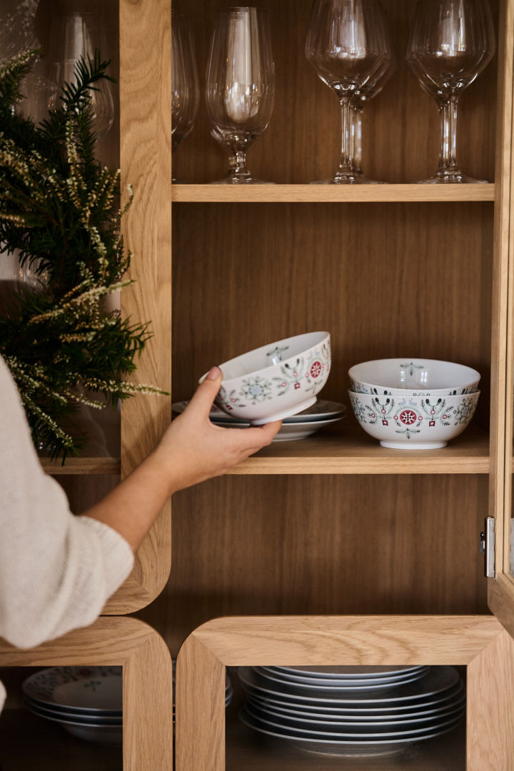 A hand removes a patterned Christmas bowl from a cupboard to be placed on a Christmas table setting. 