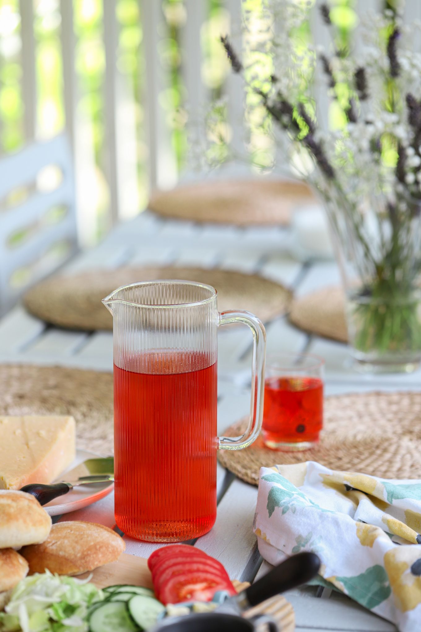 Picture showing Saga carafe from Sagaform, filled with red juice. On the table, a breakfast of rolls, sliced vegetables and cheese.