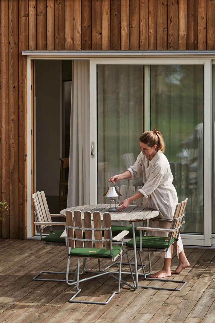 Decorated wooden deck with Grythyttan outdoor chairs and dining table / set. Woman holding portable lamp in chrome.