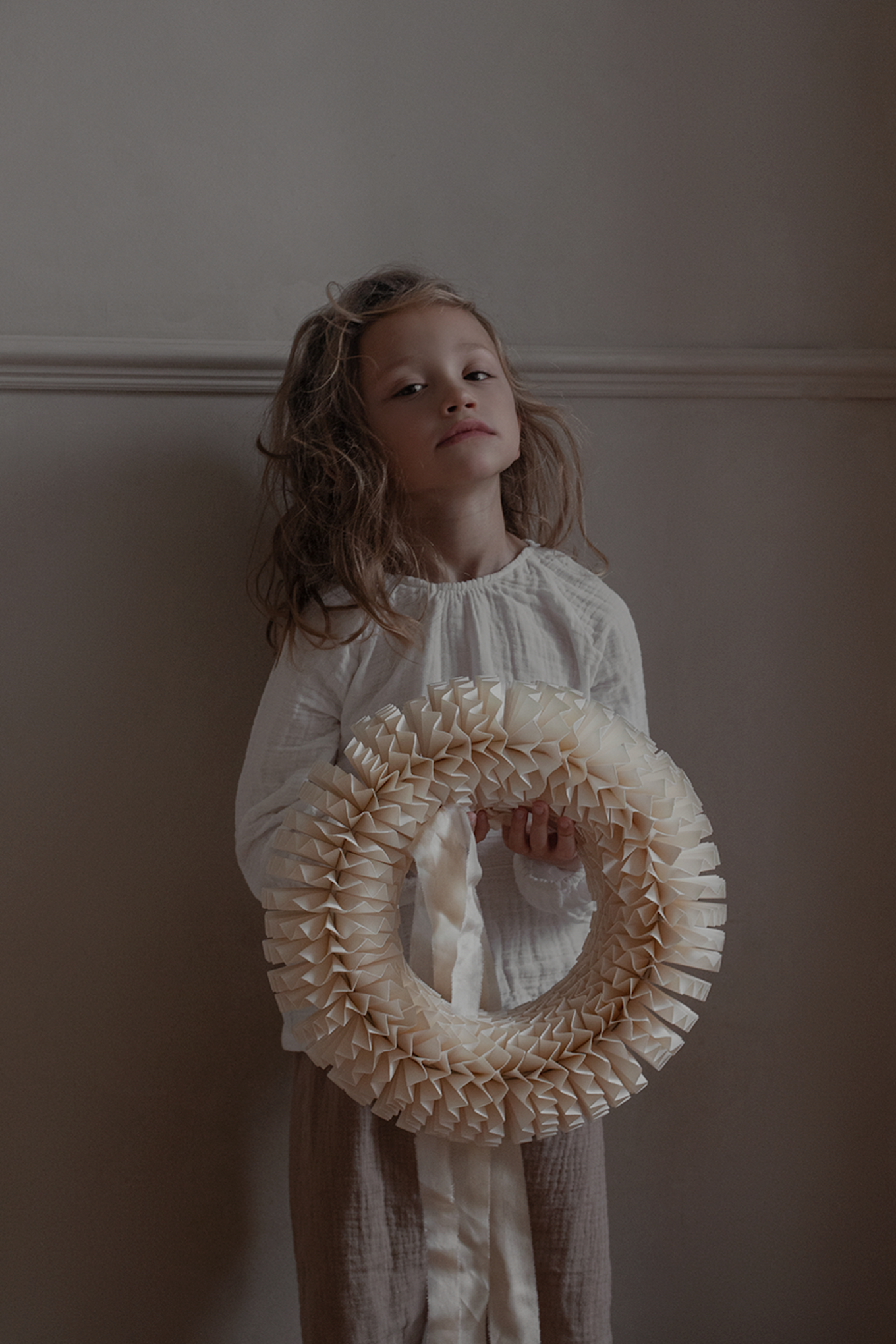 A boy holds the Stockholm wreath from Watt & Veke against a beige wall. 