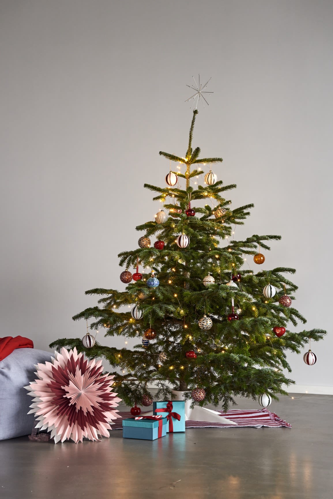 Here you see a Christmas tree decorated with colourful Christmas tree decoration ideas, next to the tree is a pink Christmas star. 