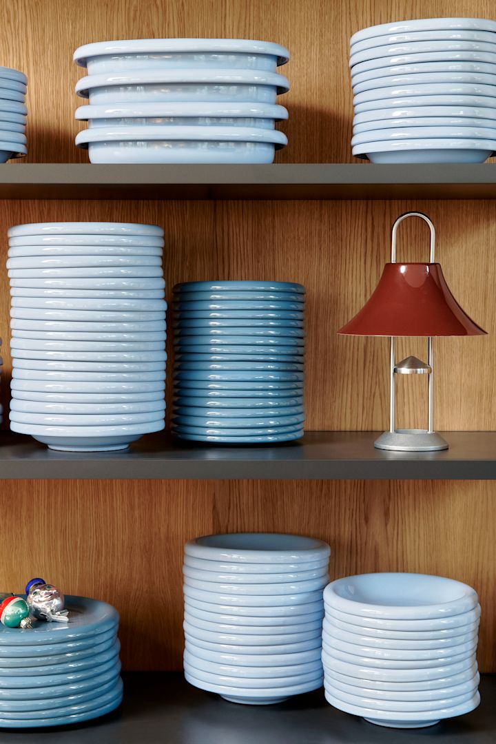 Sky blue is an important colour in the Interior colour trends 2025. Here you see a pile of barro plates from Hay stacked in a wooden shelf. 