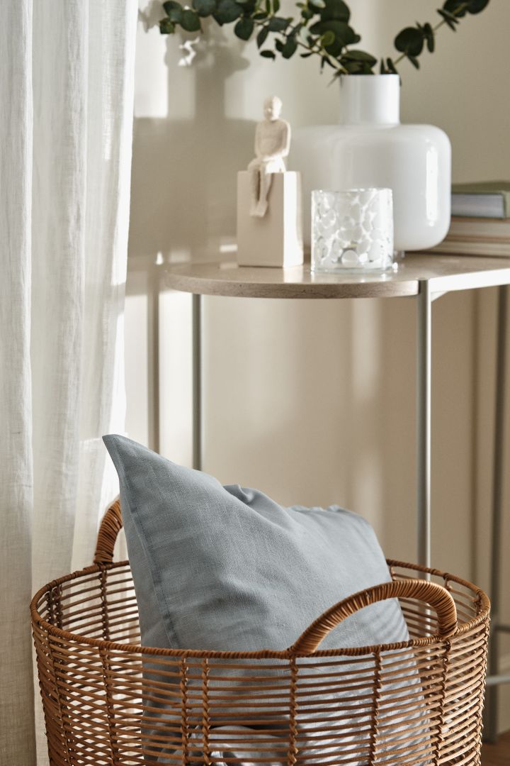 Sky blue linen cushion, lying in a basket in a beige living room.