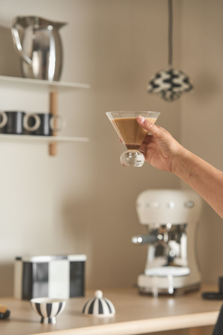 The perfect coffee bar at home naturally includes the right glasses. Here you can see a hand holding a Spice glass from Byon filled with coffee, with a coffee corner in the background.