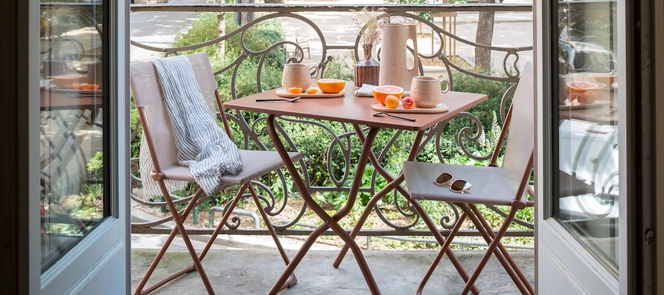 A small balcony with terracotta coloured folding chairs and tables. 