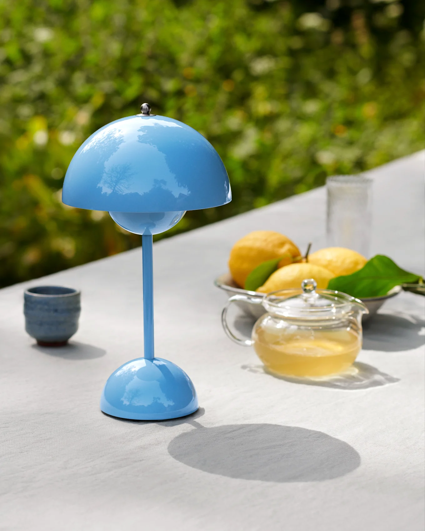 A blue mushroom-shaped table lamp on an outdoor table with a teapot, lemons, and a cup.